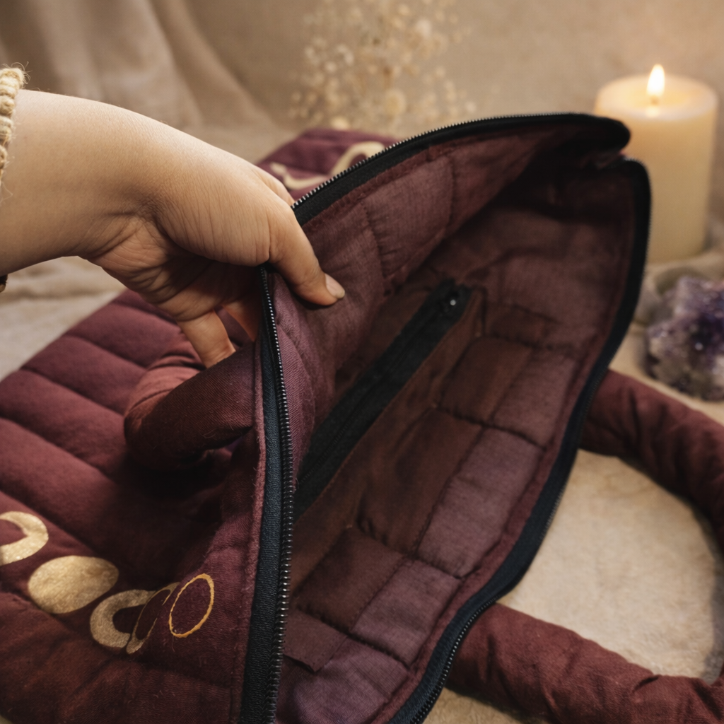 Close-up of a hand zipping up a maroon quilted jacket with a soft focus background.