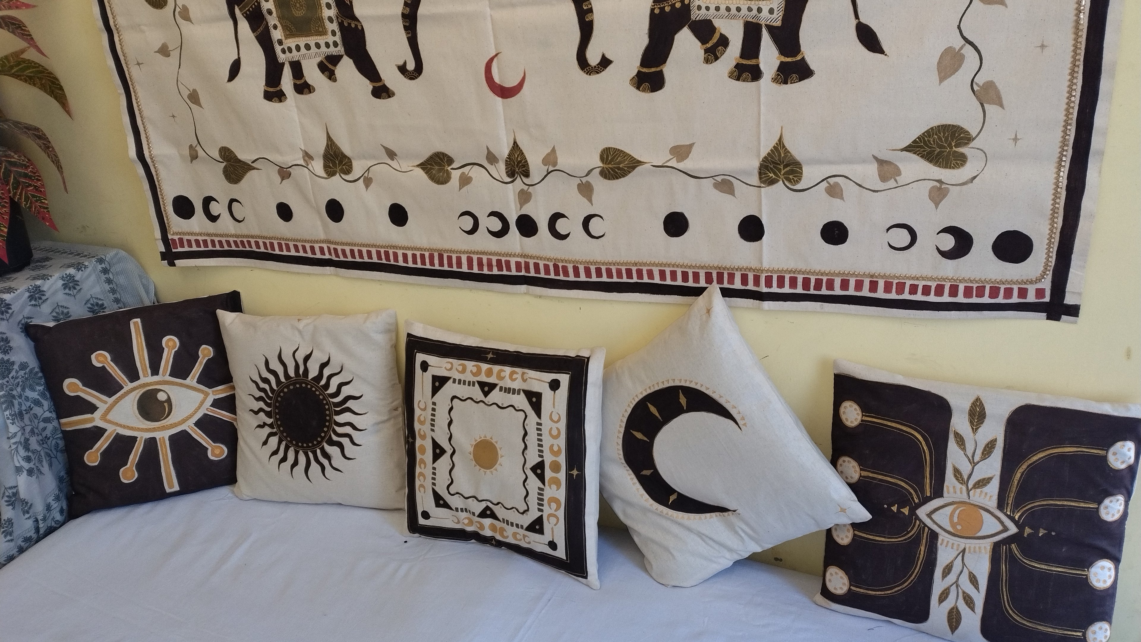 Decorative pillows with celestial designs on a couch, featuring a tapestry with elephant and moon patterns in the background.
