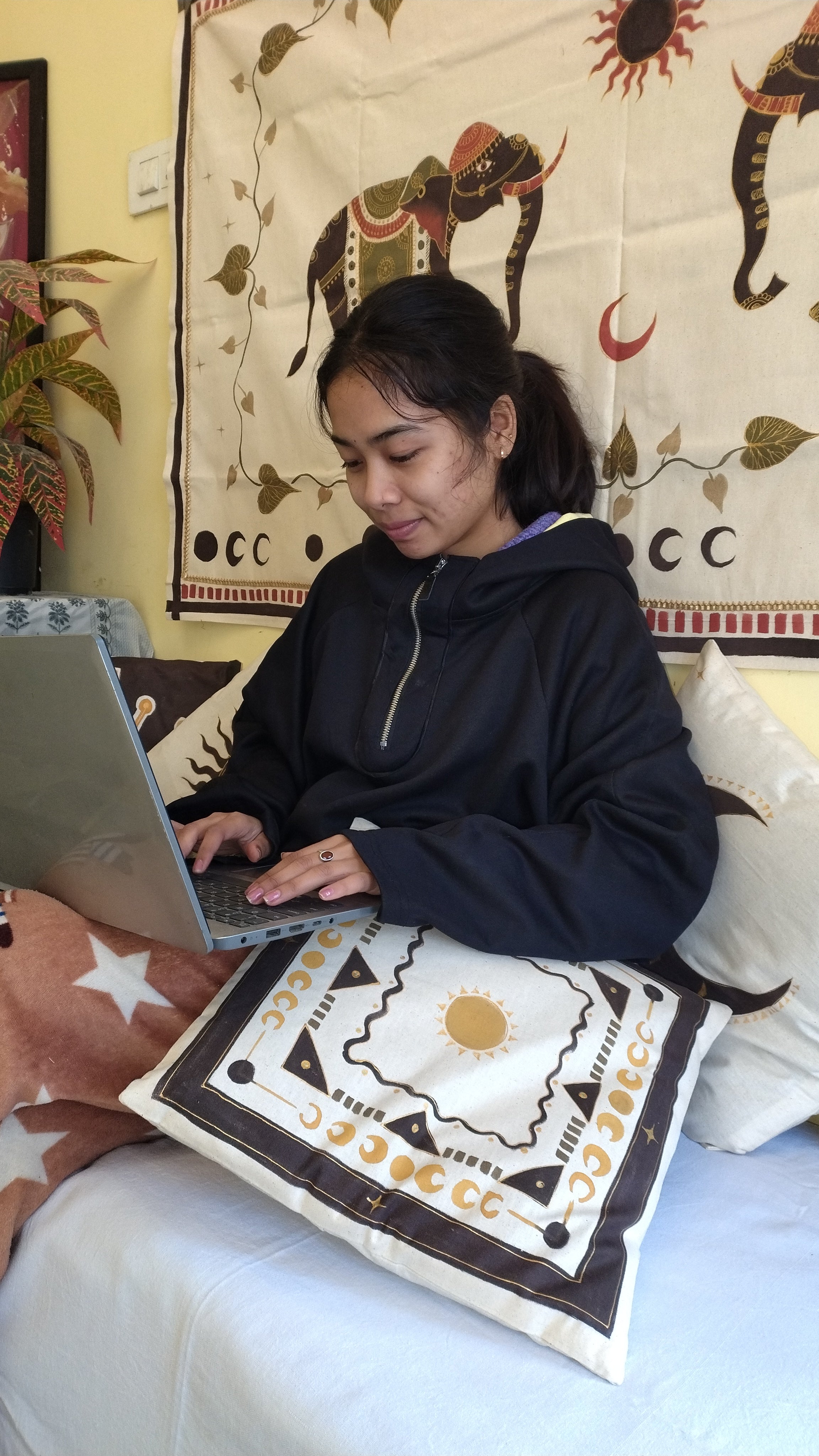 Person lying on a bed using a laptop with a colorful patterned blanket and pillow in the background.