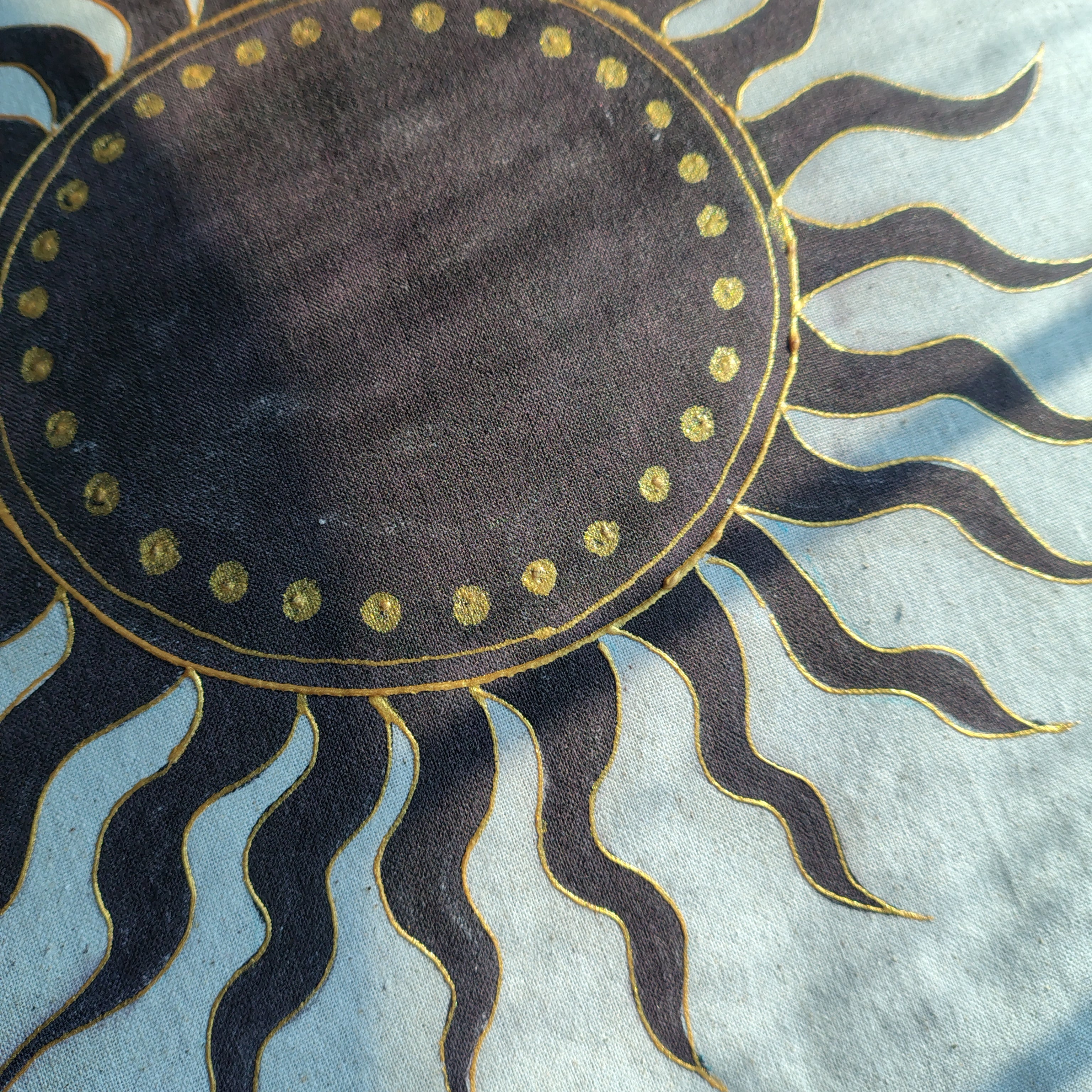 Decorative sun design with black rays and gold accents on a textured fabric background