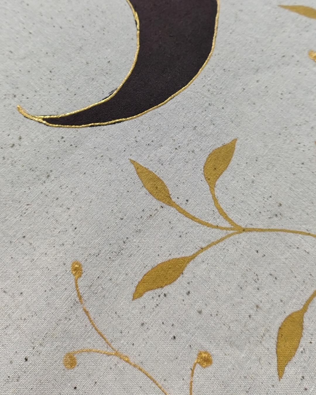 Close-up of fabric with gold leaf pattern and black crescent moon on gray background, sun and moon tapestry hand painted on fabric,