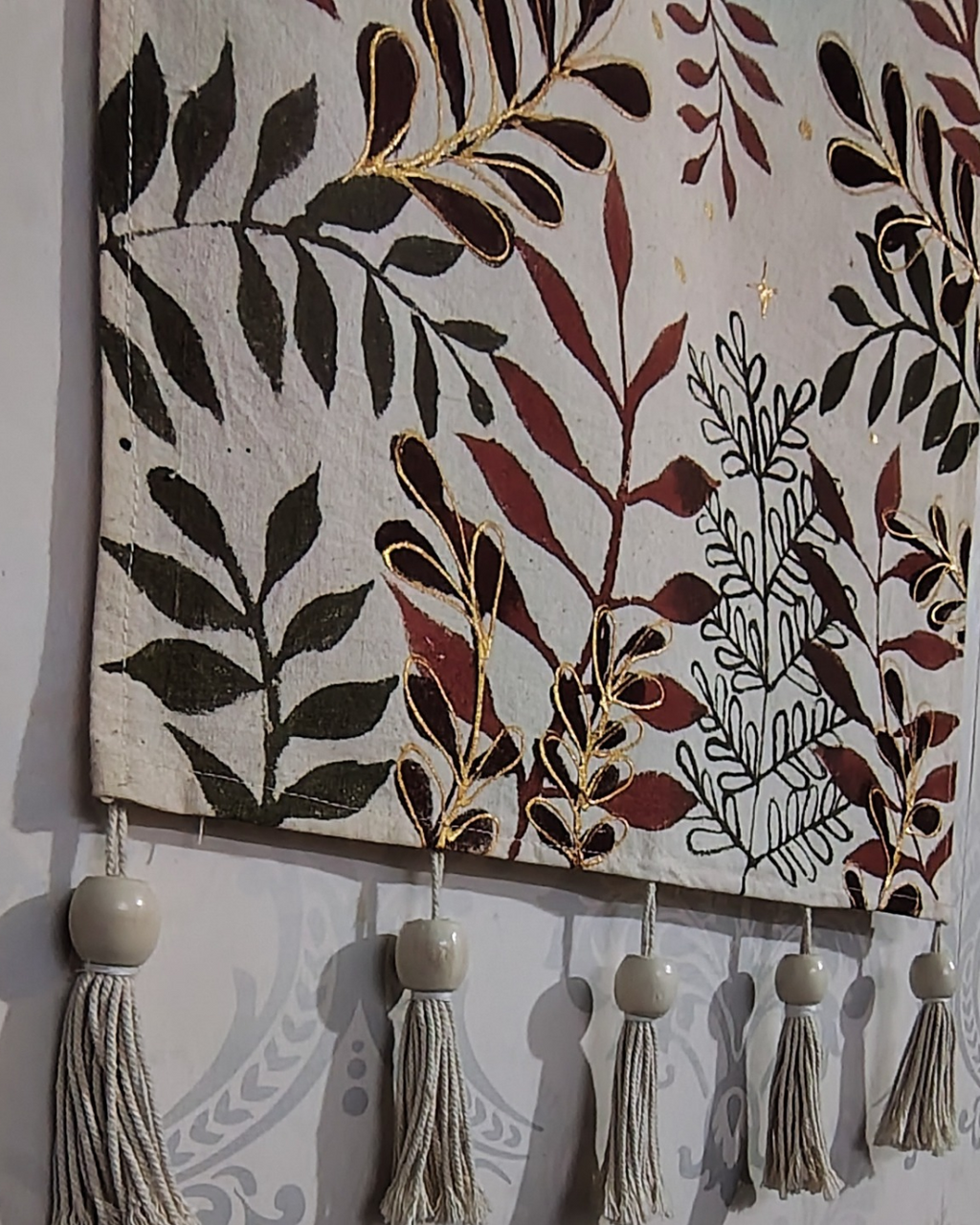 Decorative wall hanging with leaf patterns and tassels on a plain background