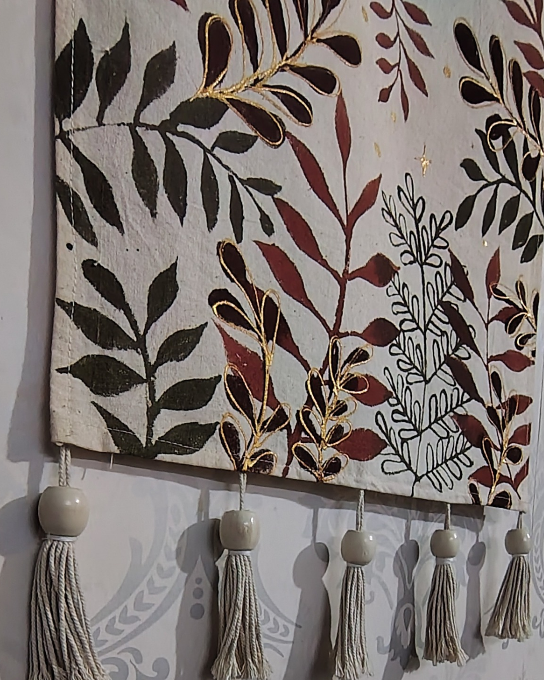Decorative wall hanging with leaf patterns and tassels on a plain background