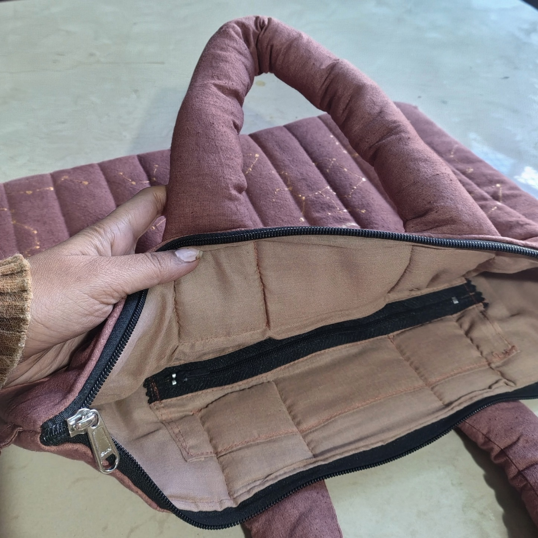Close-up of a person holding a pink quilted bag with a zipper.
