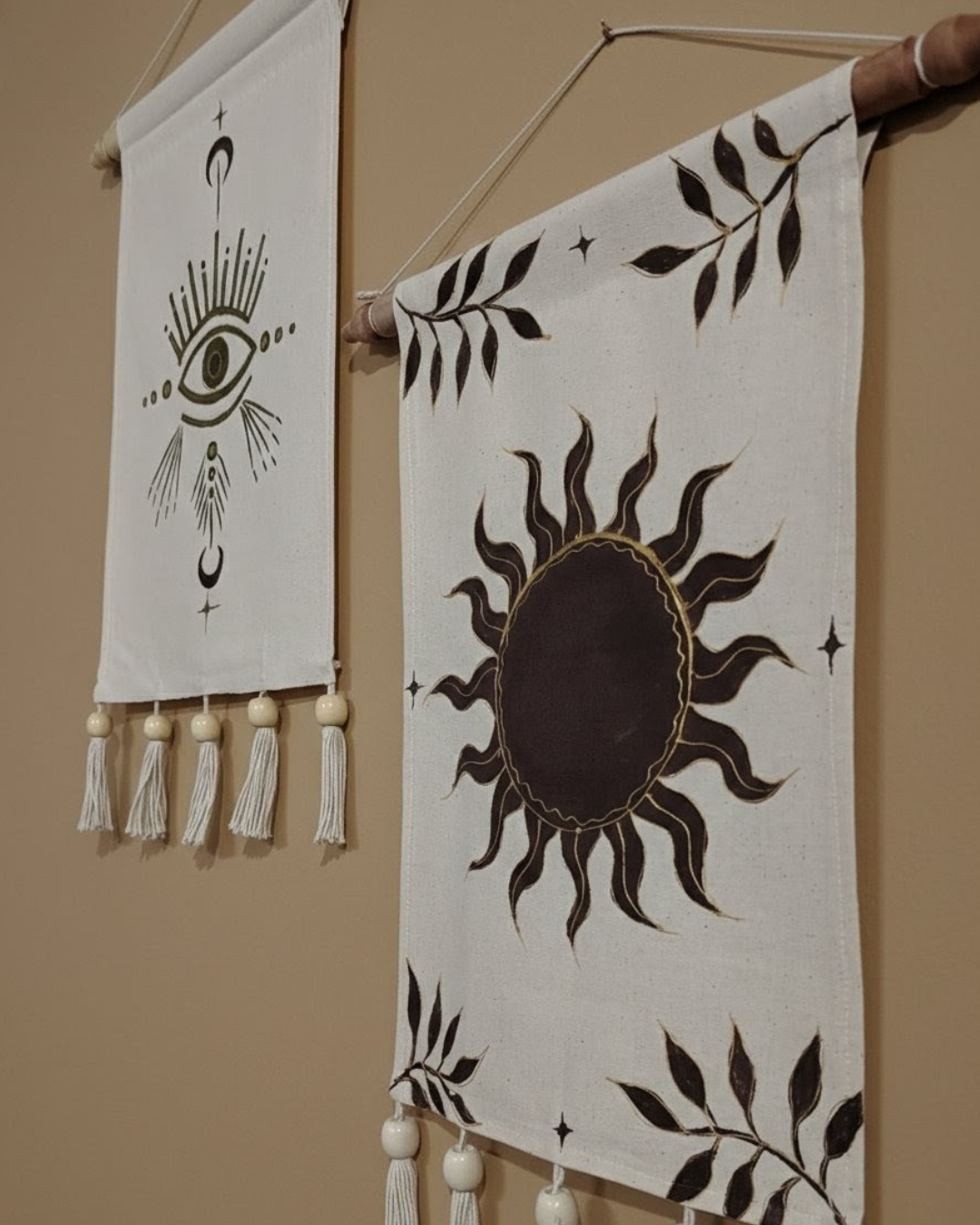 Two decorative wall hangings with celestial designs and tassels on a beige wall. hand painted room decor
