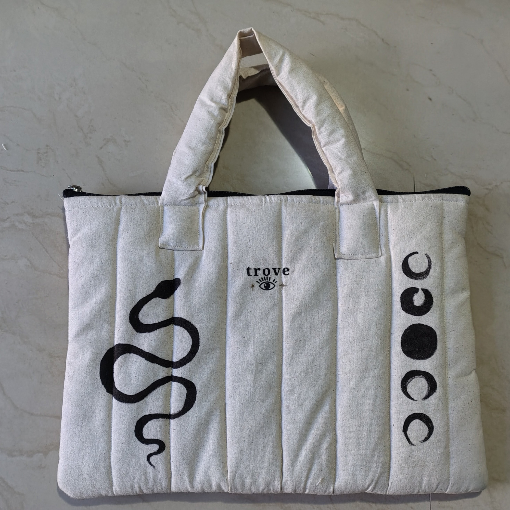 White tote bag with black snake design and 'trove' branding on a light gray background, puffy laptop bag, hand painted sake laptop pouch, new and unique office laptop pouch.