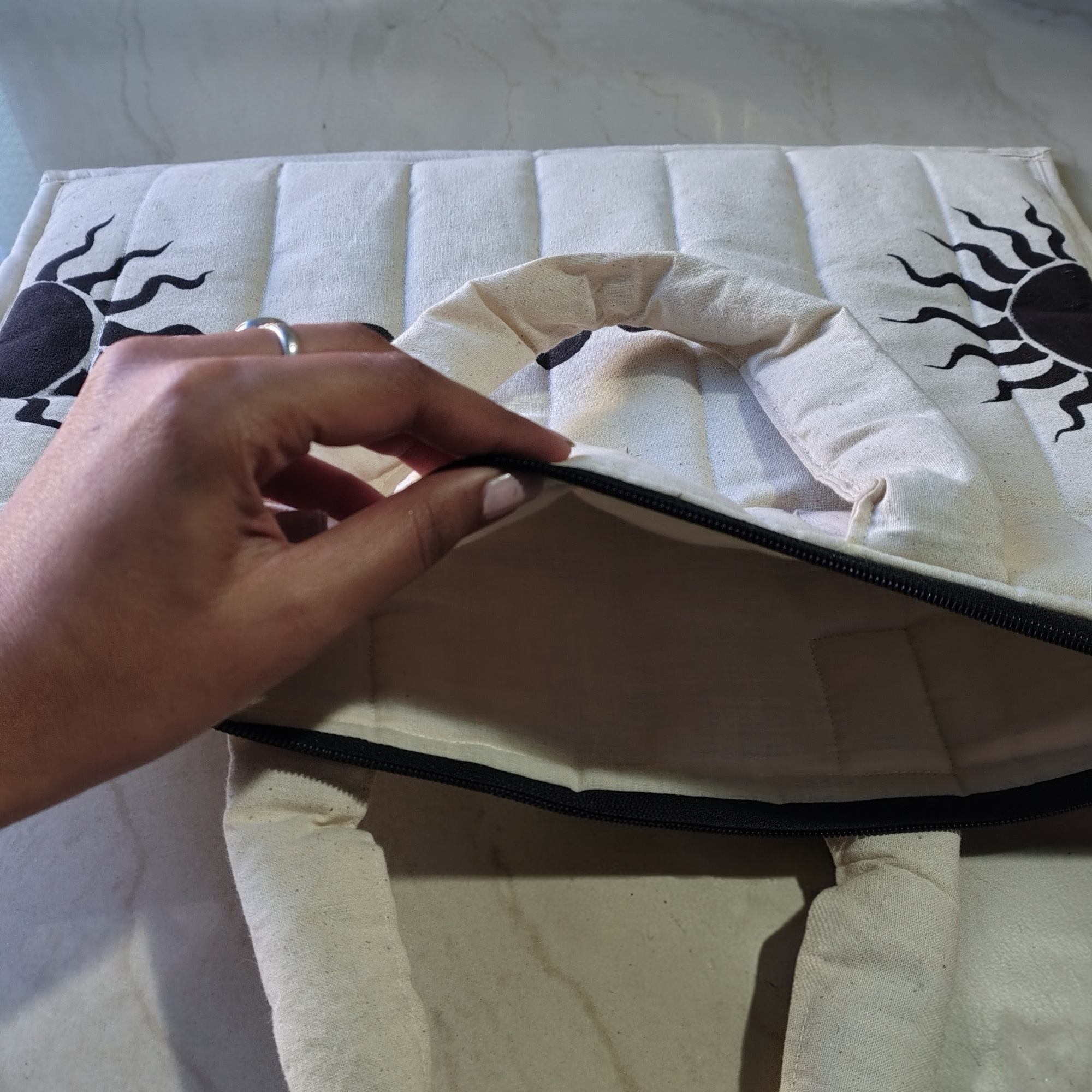 Hand zipping a white cushion with black sun designs on a light background, hand painted sun and moon phase laptop bag, puffy and quilted laptop bag for office and college purpose