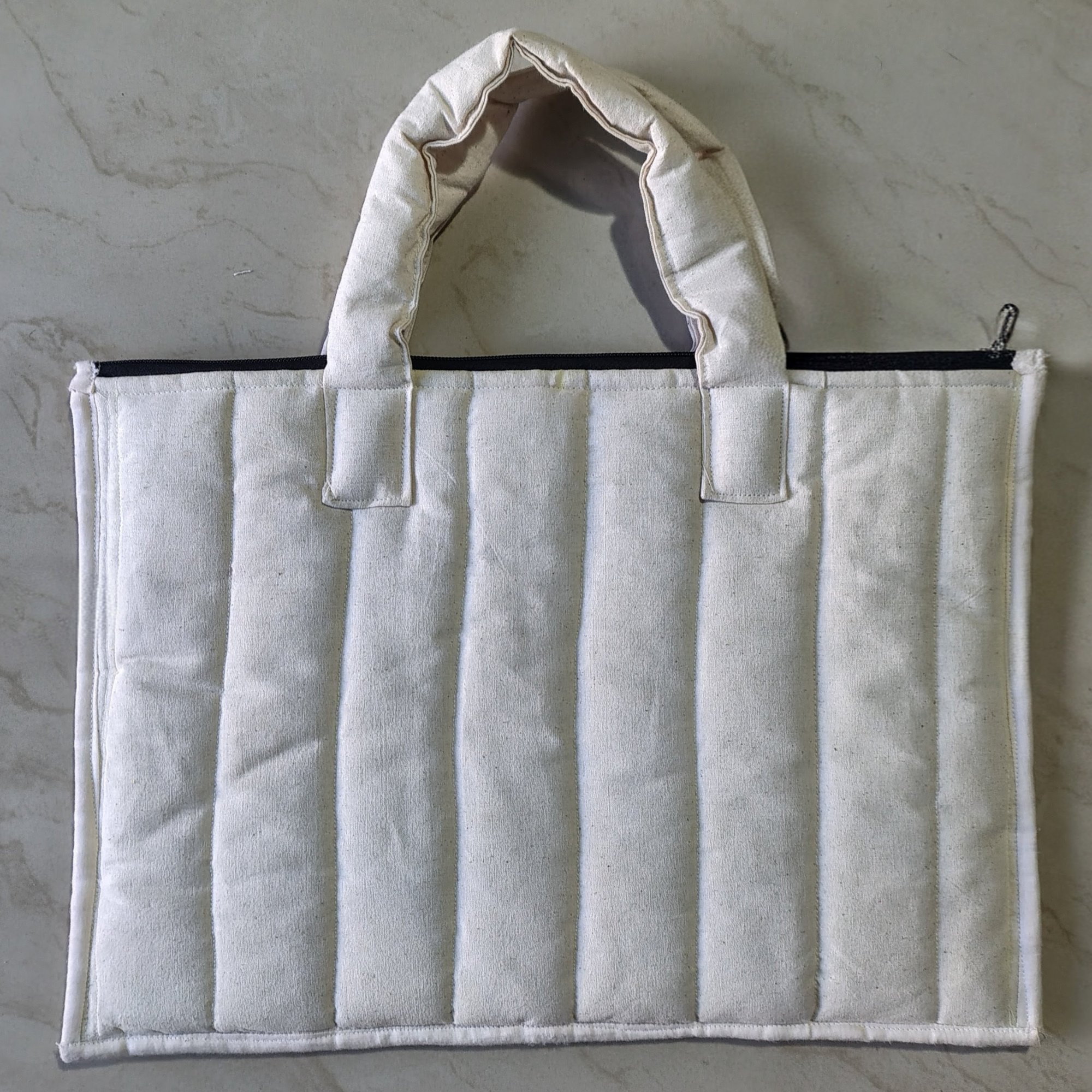 White quilted bag with a zipper on a gray background