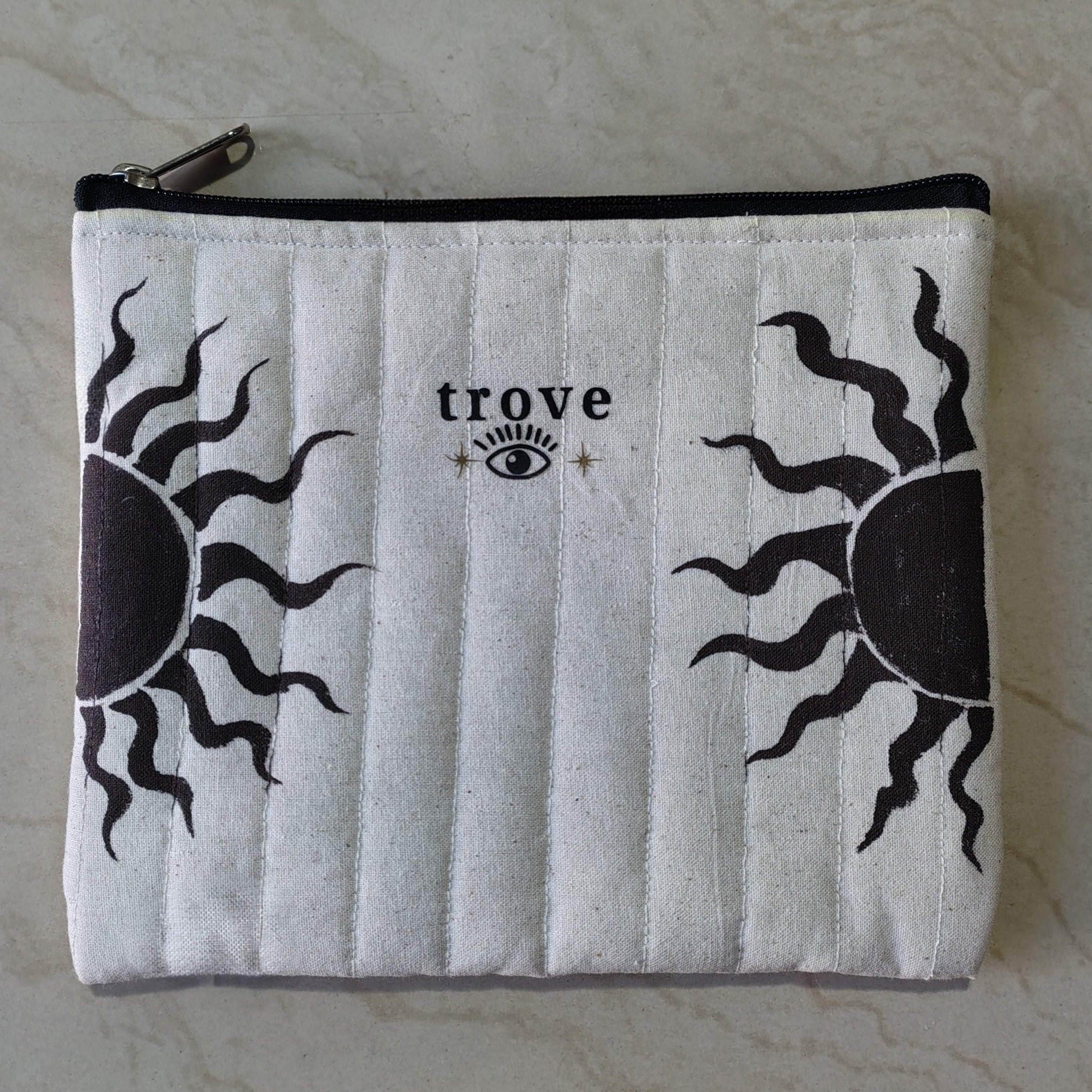 White pouch with black sun designs and 'trove' branding on a marble surface hand-painted