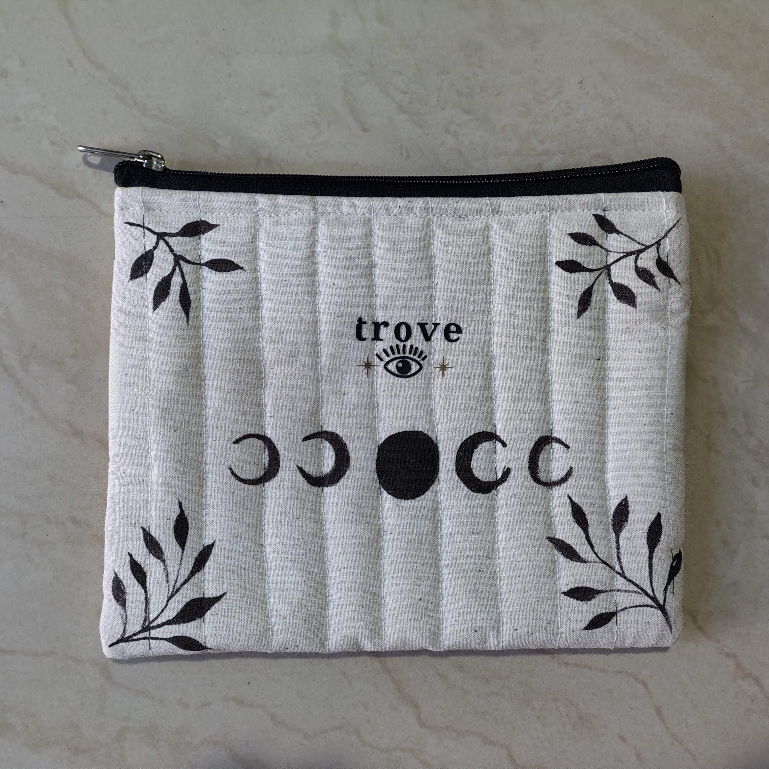 White pouch with black designs and 'trove' branding on a marble surface, hand painted and hand made, moon phase, spiritual, makeup pouch