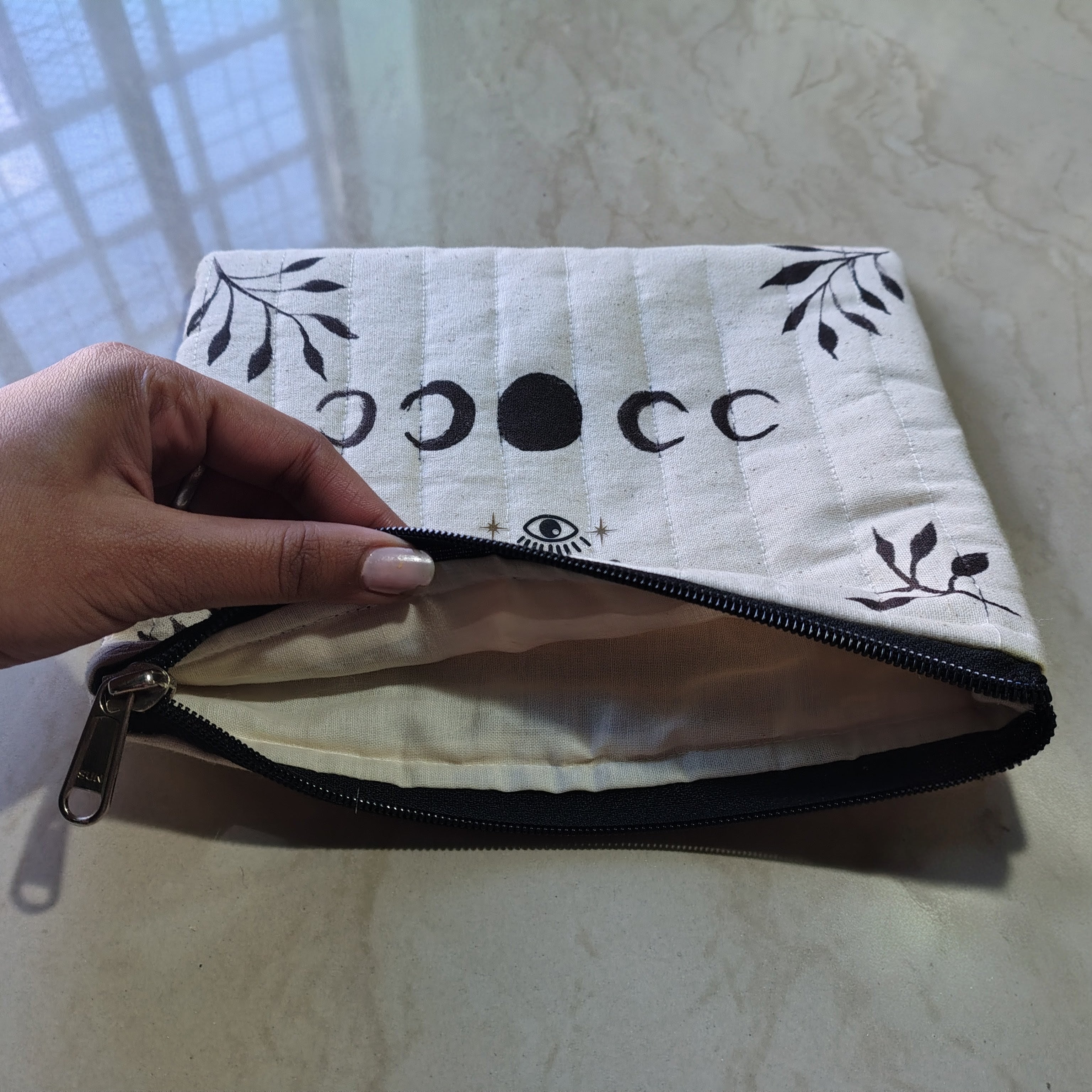 Hand holding a white pouch with black designs on a light background, moon pase spiritual makeup pouch.