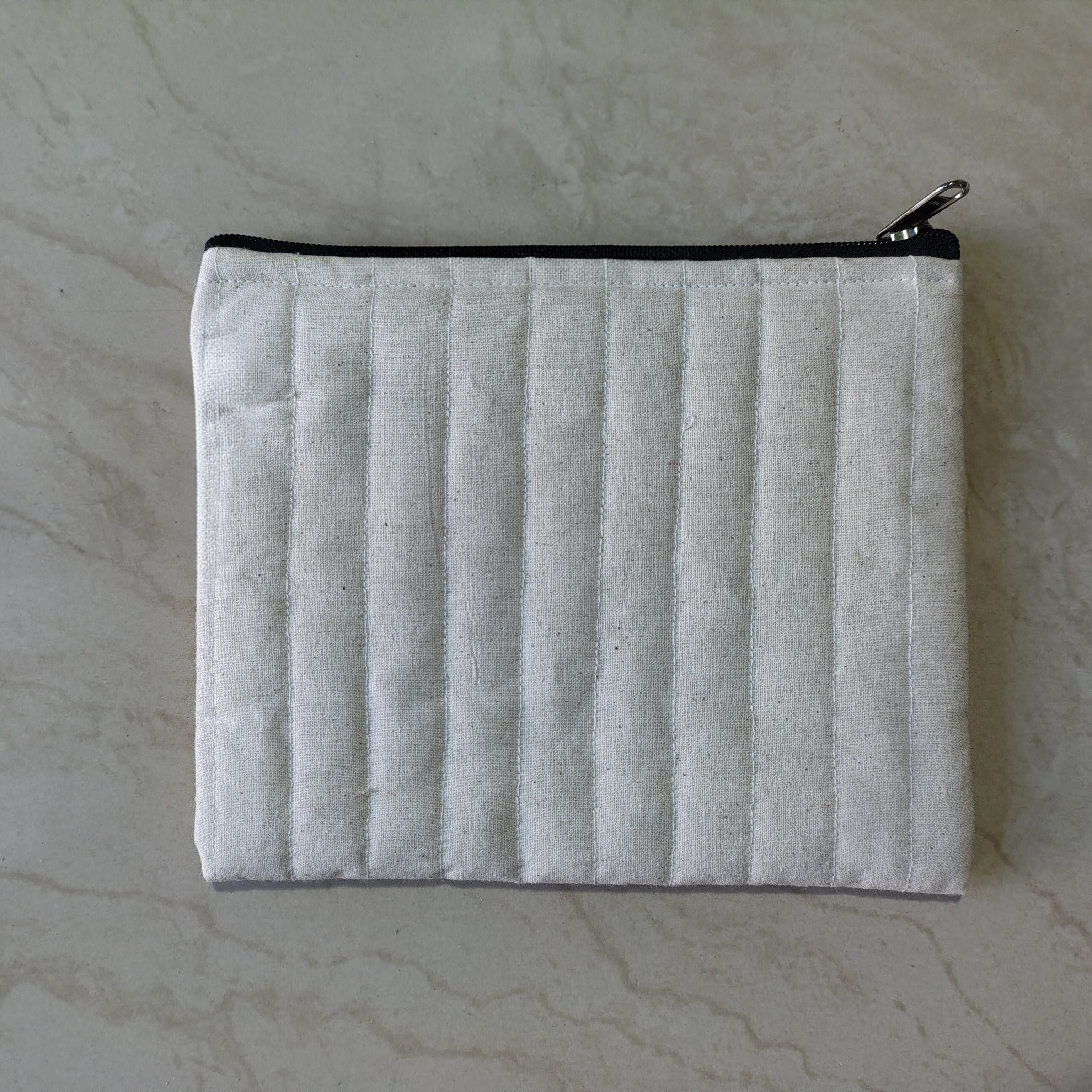 White quilted pouch with a black zipper on a marble surface