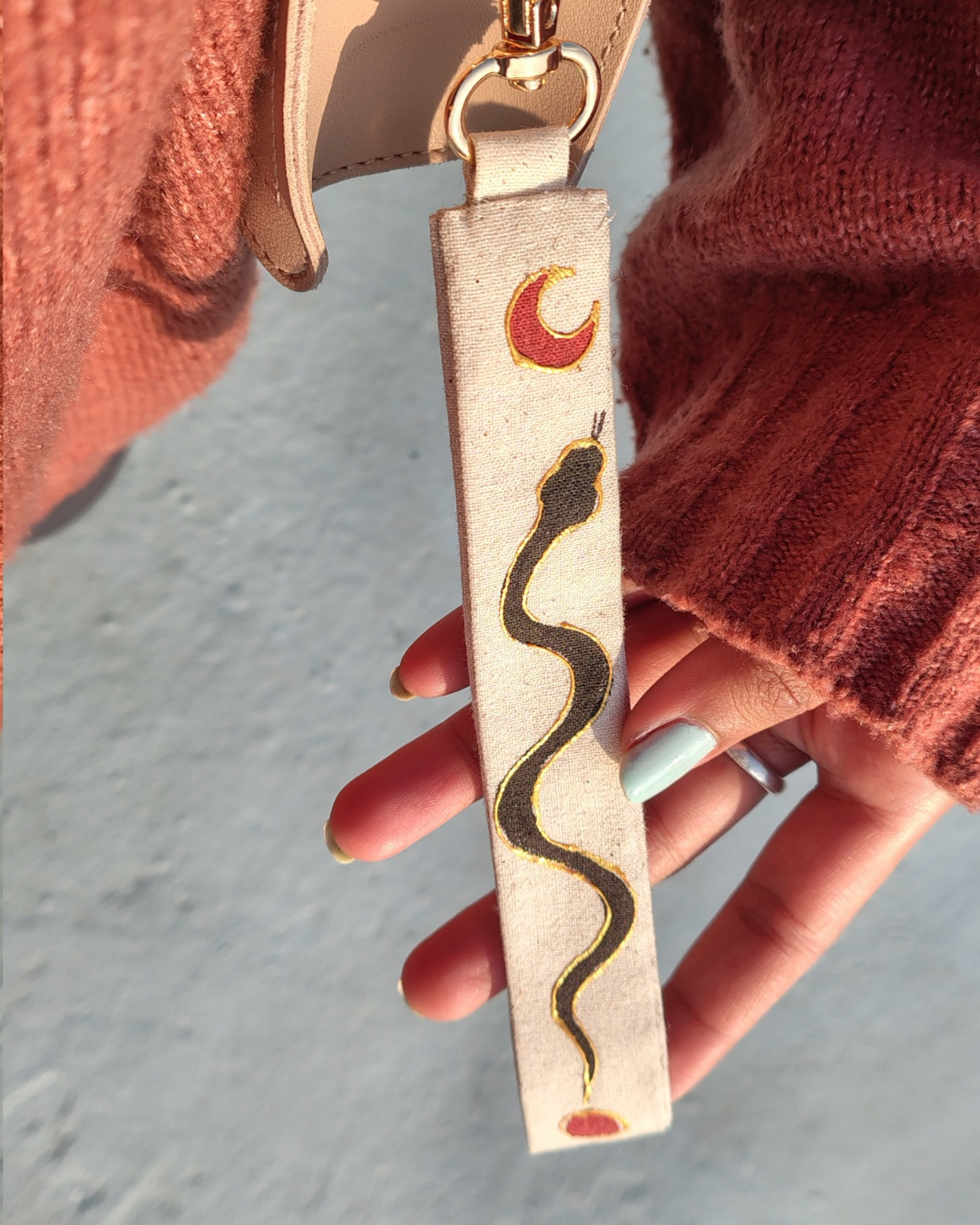 Keychain with snake design held by a person wearing a red sweater. key chain , bag accessory