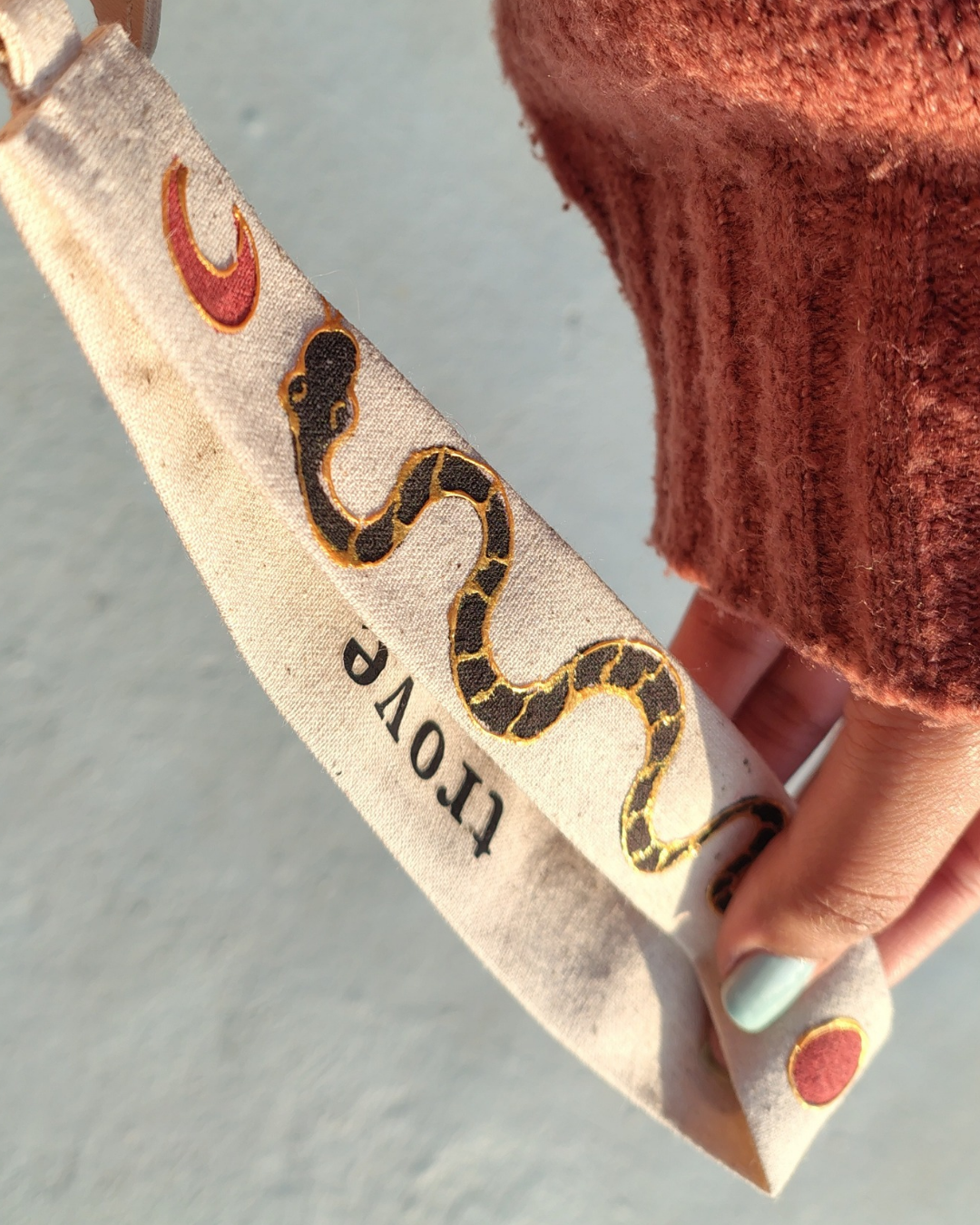 Textured beige strap with snake design and 'trove' text, held by a person wearing a brown sleeve. bag accessory, key chain.